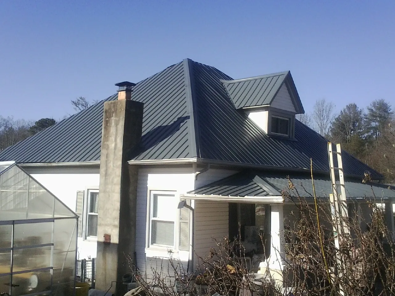 Dark blue standing seam metal roof on a white farmhouse with dormer — Slate & Tile Roof Repair by Roofing Brothers in Sunapee
