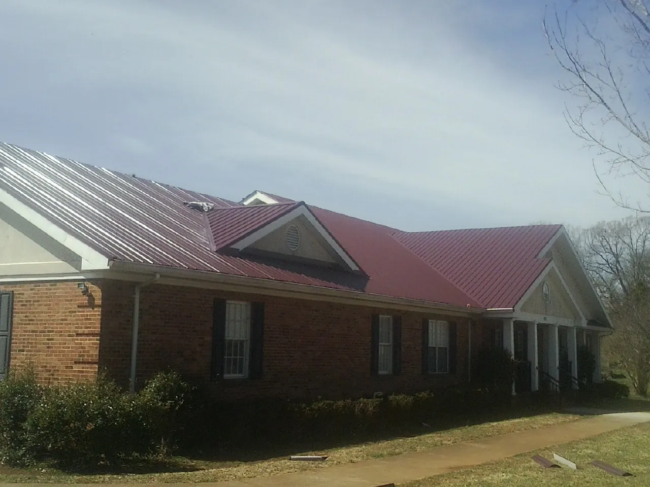 Red metal roof with gabled entries on a long brick building, from a Hail Damage Roof Repair job in Sunapee
