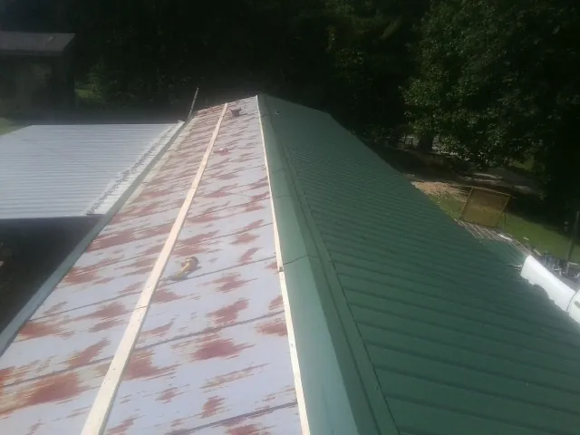 Old rusted panels beside newly installed green metal roofing — Wind Damage Roof Repair by Roofing Brothers in Sunapee