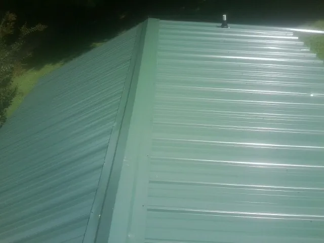 New green metal panels meeting at the ridge of a roof — Flat Roof Repair work by our crew in Sunapee