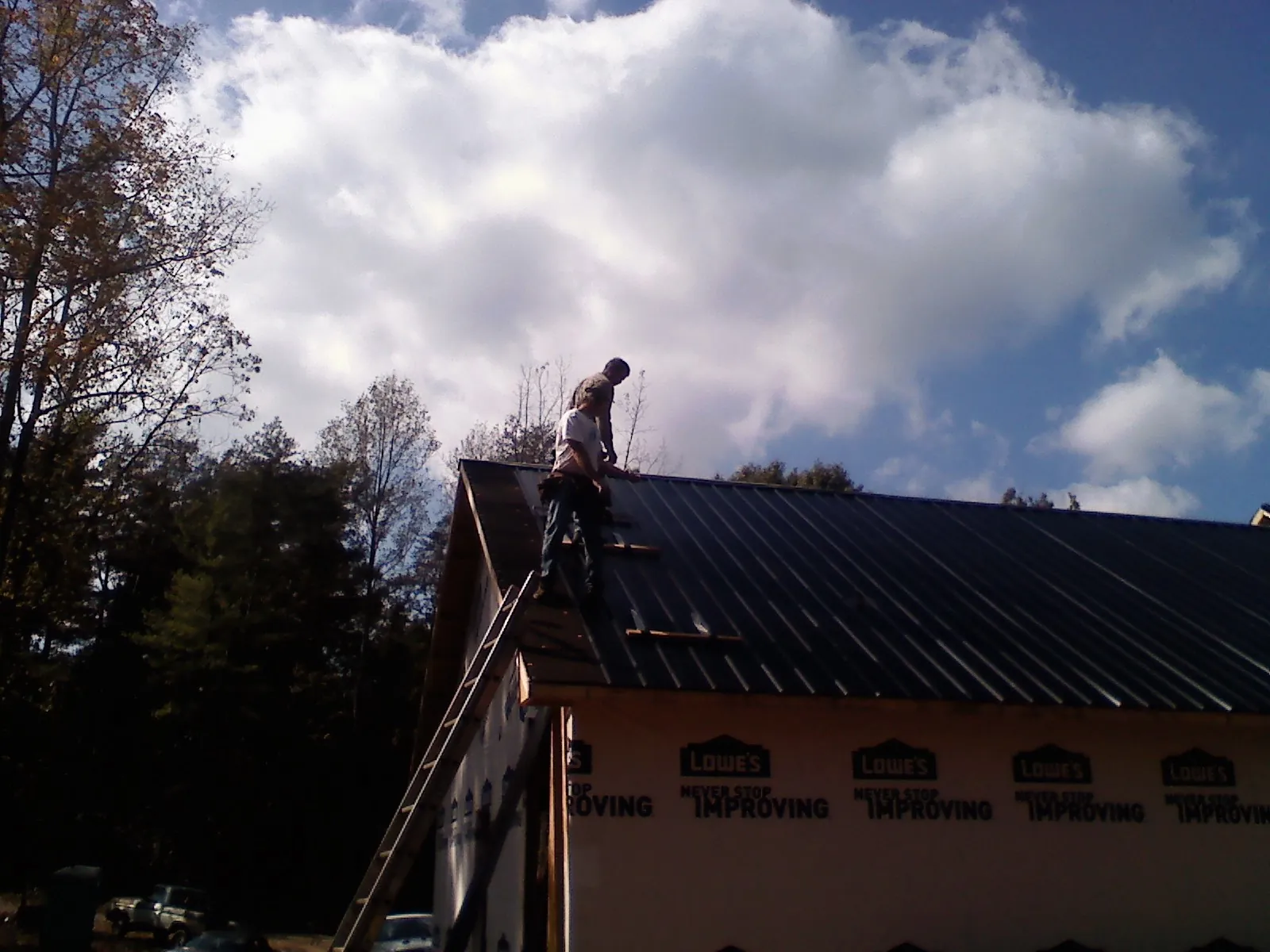 Roofer fastening dark metal panels high against a cloudy sky, from a Roof Inspection job in Sunapee