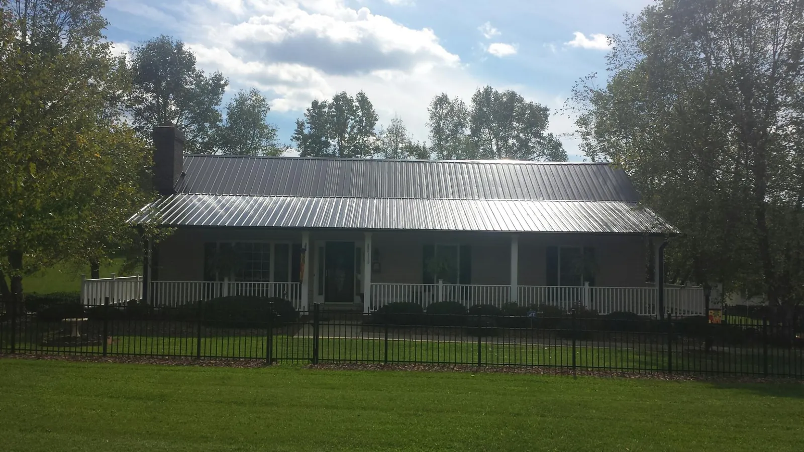 Gray metal roof on a brick ranch with a full width front porch — Gutter Guard Installation work by our crew in Sunapee