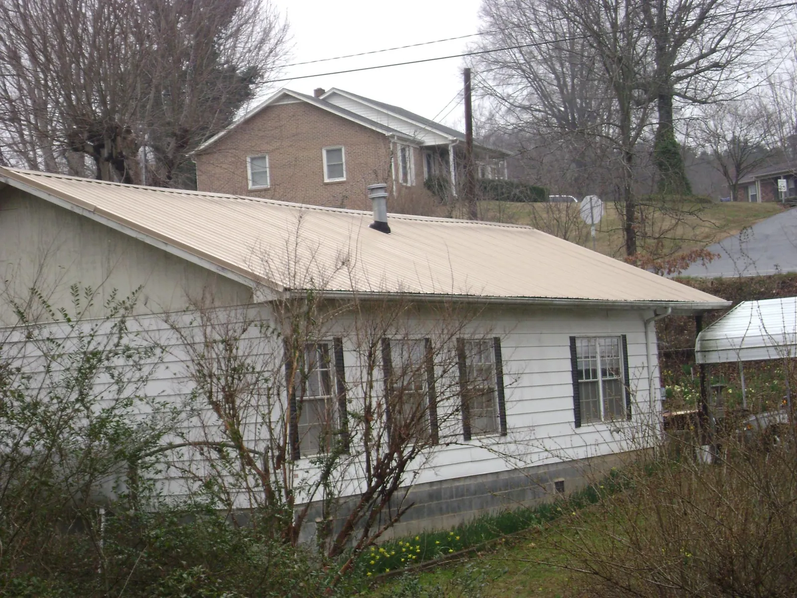 Tan metal roof on a white sided house set into a hillside — Commercial Roofing by Roofing Brothers in Sunapee