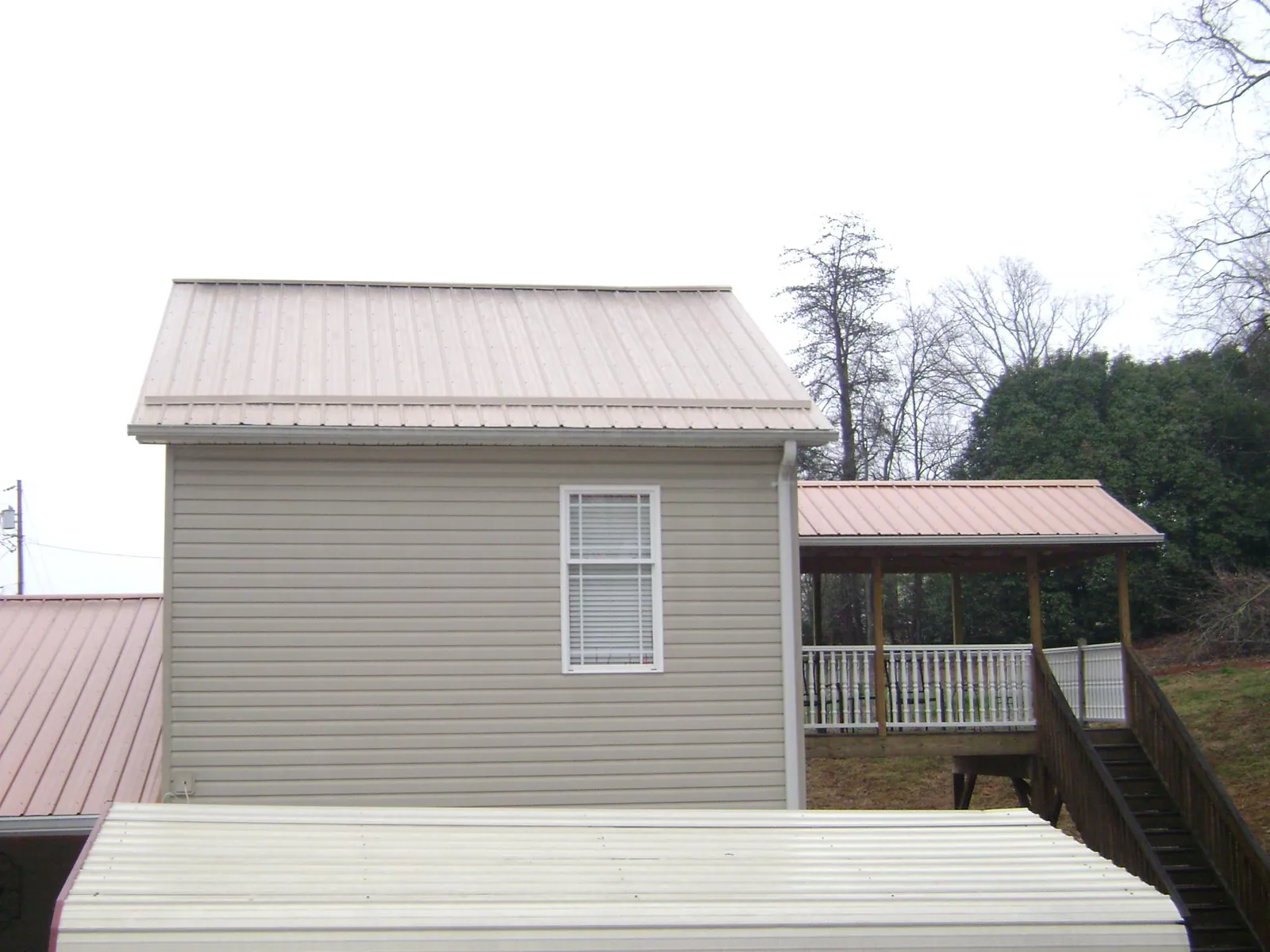 Tan metal roofs on a two story addition and attached porch, from a Roof Replacement job in Sunapee