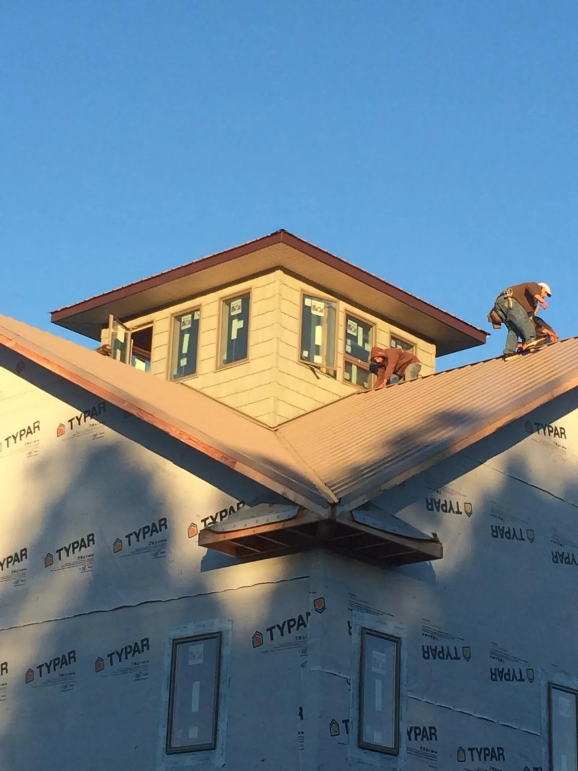 Roofers working around a rooftop cupola on a new metal roof at sunset — Roof Waterproofing in Sunapee by Roofing Brothers